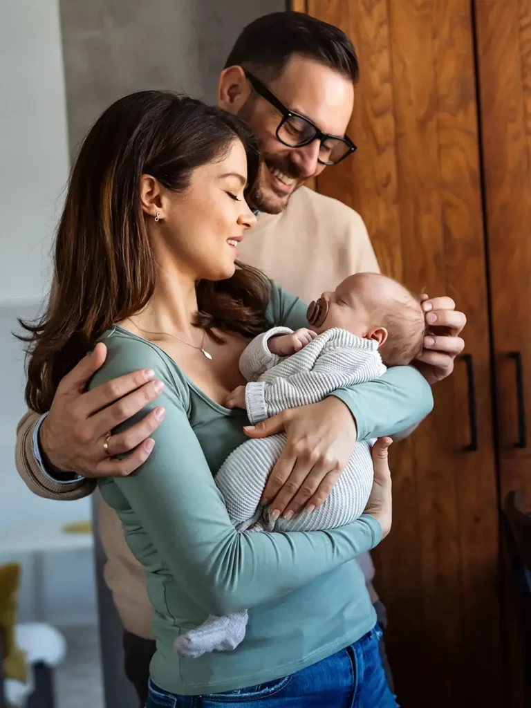 Portrait of young happy man and woman holding newborn cute babe dressed in white unisex clothing. Caucasian smiling father and mother embracing tenderly adorable new born child. Happy family concept