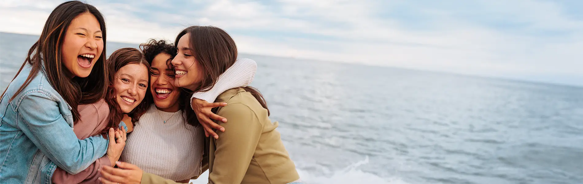 Portrait of four young women laughing and hugging on beach